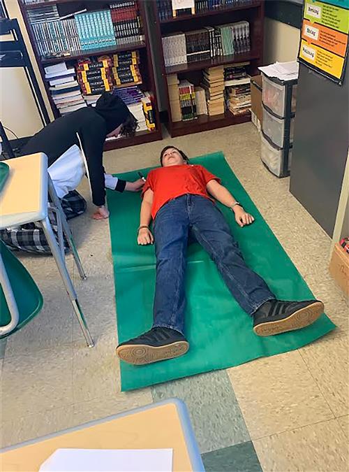 Student drawing a life-size outline of another student.